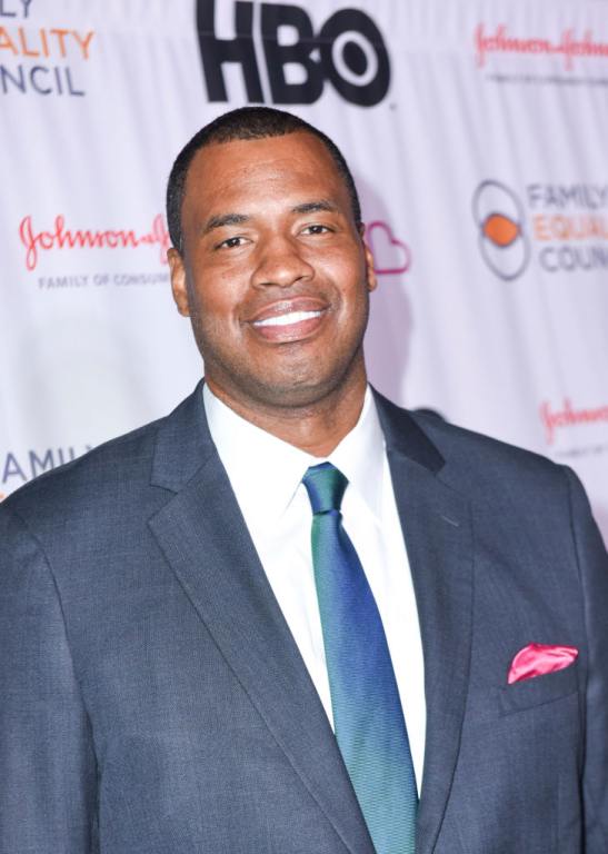 Jason Collins smiling wearing a blue suit and tie.