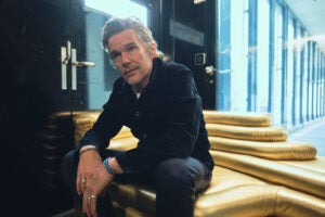 Ethan Hawke poses for a portrait session before the "ZFF Masters: Ethan Hawke" during the 19th Zurich Film Festival sitting on steps hunched over wearing jeans and a black shirt.