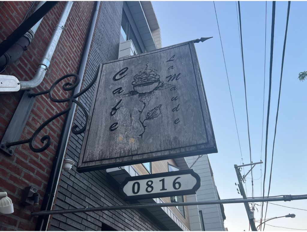 Photo of the unassuming wooden sign hanging out in front of Cafe La Maude in Philly. The restaurant made the Yelp Top 100 Brunch Spots of 2024 List.