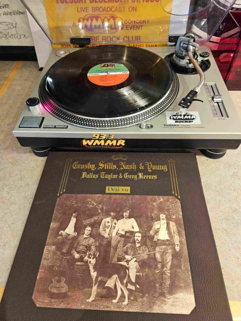 The vinyl record of Crosby, Still Nash and Young "Deja Vu" on a turntable with the album cover laying on the table below it